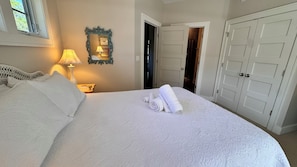 A neatly made bed with a rolled towel, a bedside lamp, and a mirror on the wall.