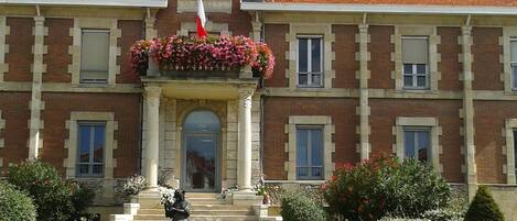 A building with a clock, a statue, and a flower bed in front.