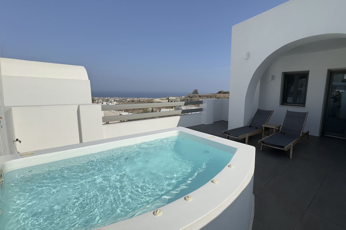 A rooftop pool area with a hot tub, lounge chairs, and a view of the sea.