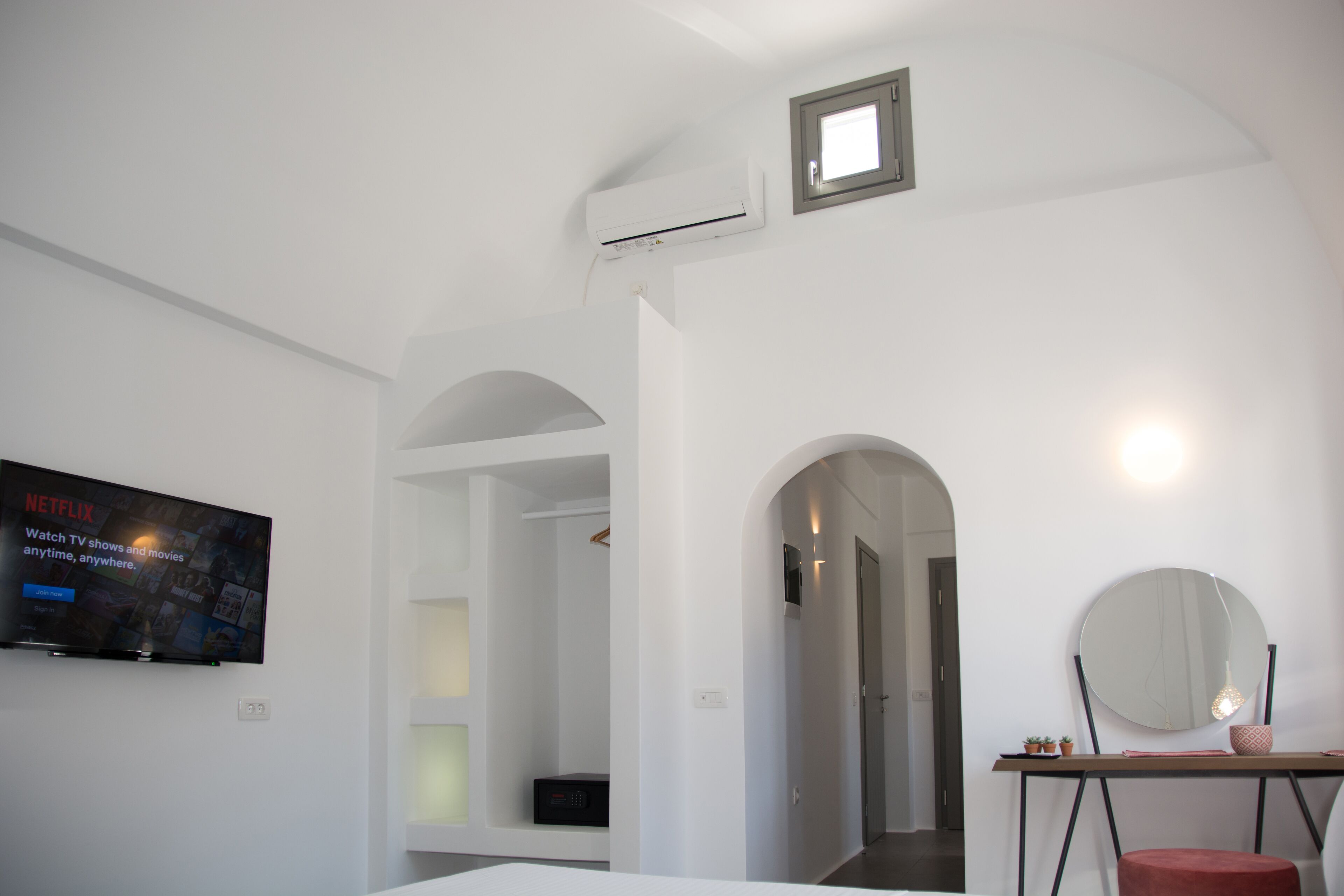A modern, minimalist hotel room with a flat-screen TV, a round mirror, and a small table.