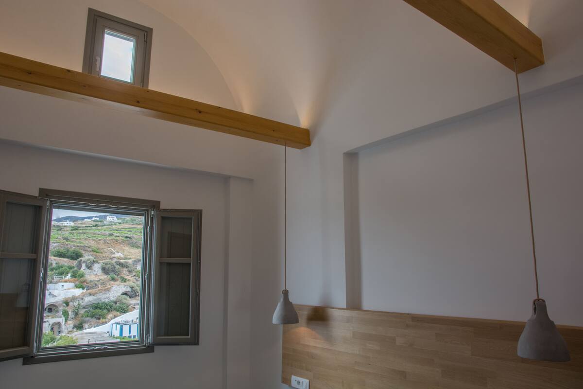 A room with a wooden ceiling beam, a window with a view of a landscape, and two pendant lights.