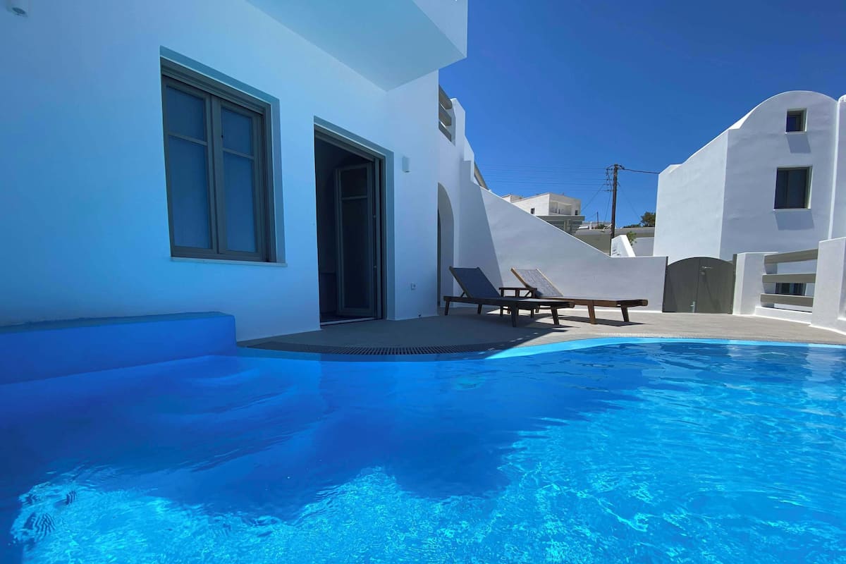 A clear blue swimming pool with lounge chairs and a white building with large windows.