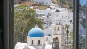A view through an open window of a coastal town with white buildings and blue domes, likely a tourist destination. - Amphitrite Suites Santorini (Santorini)