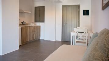 Un espacio habitable compacto con kitchenette, comedor y una puerta que da a otra habitación.