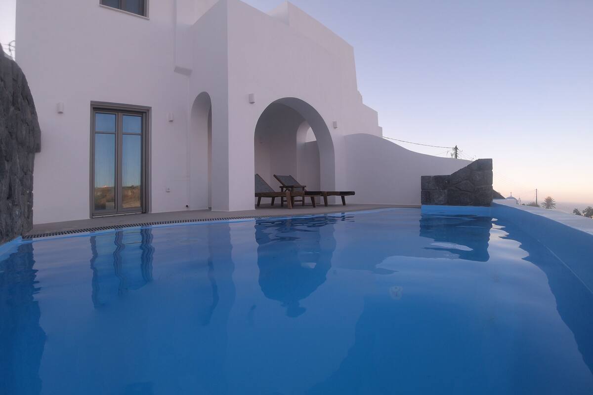 A modern building with a swimming pool, a stone wall, and a clear sky.