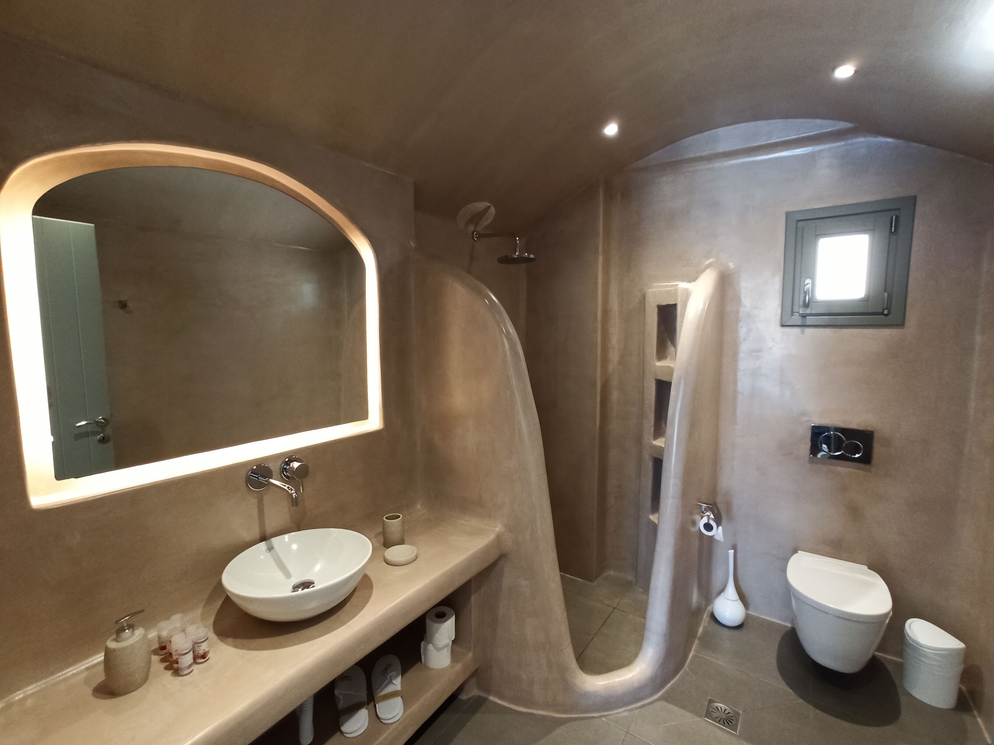 A modern bathroom with a curved shower, a large mirror, and a toilet.
