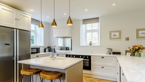 A modern kitchen with a central island, bar stools, stainless steel appliances, pendant lighting, and a view of the outdoors.