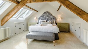 A bedroom with a sloped ceiling, a bed with a grey upholstered headboard, a bench, bedside tables, and a radiator.