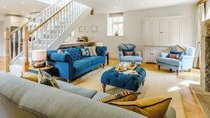 A spacious living area with a staircase, a blue sofa, a blue armchair, and a wooden coffee table.