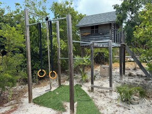A wooden play structure with a rope swing and a small wooden house.