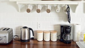 Et køkken med hvide skabe, en træbordplade, kaffemaskine, elkedel og brødrister.