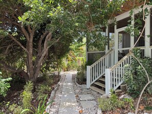 A pathway leading to a wooden staircase with a white railing, surrounded by lush greenery and trees. - Very Large Studio & Porch, 5 Min Walk to Beach, Secluded, Tranquil & Green (Long Bay Hills)