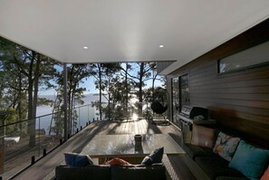 A modern interior with a glass balcony overlooking a body of water, a dining table, and a sofa with cushions.