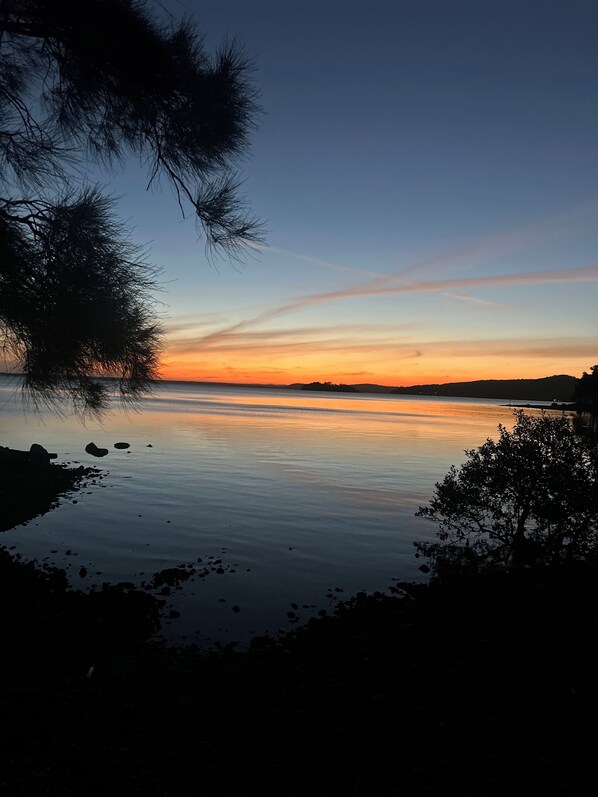 A calm lake at sunset with a clear sky and silhouettes of trees.
