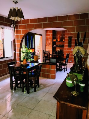 Un comedor con pared de ladrillo, una mesa con sillas, una lámpara colgante y una ventana con cortina.
