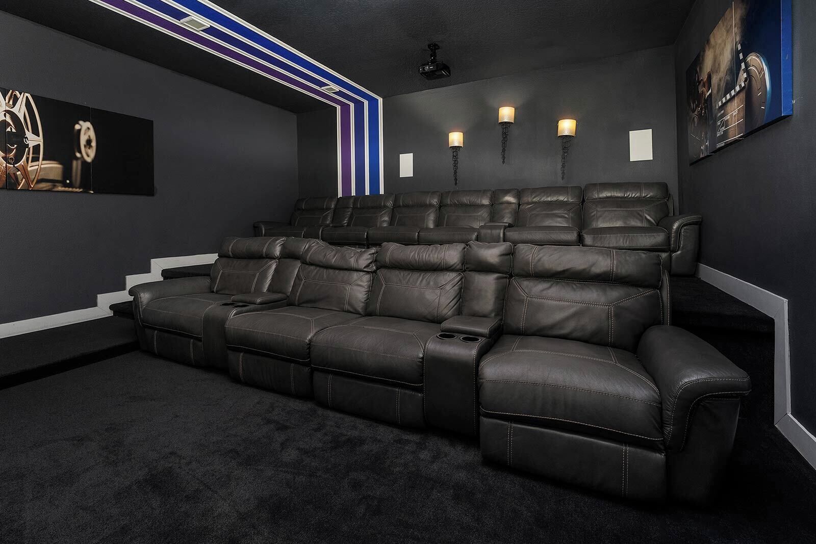 Un cine en casa con un sofá seccional reclinable, una pantalla de proyector y parlantes instalados en la pared.