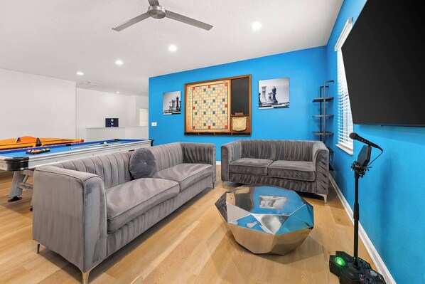 A modern living room with a pool table, two grey sofas, a coffee table, and a ceiling fan.