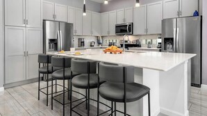 Une cuisine moderne avec des meubles blancs, des appareils en acier inoxydable et un îlot central doté de tabourets de bar.
