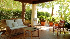 Un porche cubierto con muebles de mimbre, una mesita y plantas en macetas.