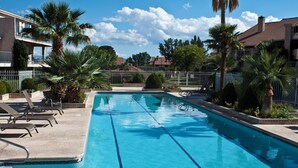 Une piscine rectangulaire à l’eau d’un bleu cristallin, entourée d’une clôture blanche et de palmiers.