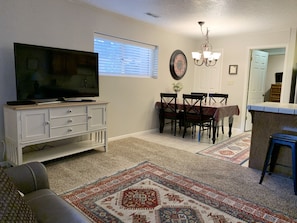 A living room with a television, a dining area with a table and chairs, a chandelier, and a patterned rug.
