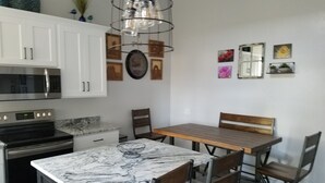 Una cocina con armarios blancos, un microondas de acero inoxidable, una estufa y una encimera de mármol. Hay una mesa de madera con cuatro sillas.