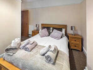 A neatly made bed with towels, two bedside lamps, a wooden headboard, a wooden nightstand, and a radiator. - 4 bedroom accommodation in Bassenthwaite, near Keswick (Bassenthwaite, near Keswick)
