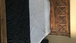 Een slaapkamer met een zwart beddegoed, een geruit plaid en een houten garderobe met geometrische patronen.