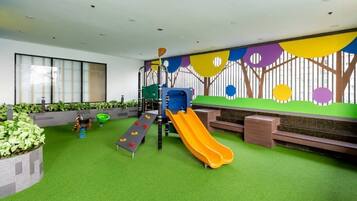Children can play on the slide and climbing frames set on a green artificial turf floor within this enclosed play area.