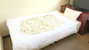 Una cama individual con una colcha estampada, una almohada blanca, un televisor sobre un soporte de madera y una lámpara junto a la cama.