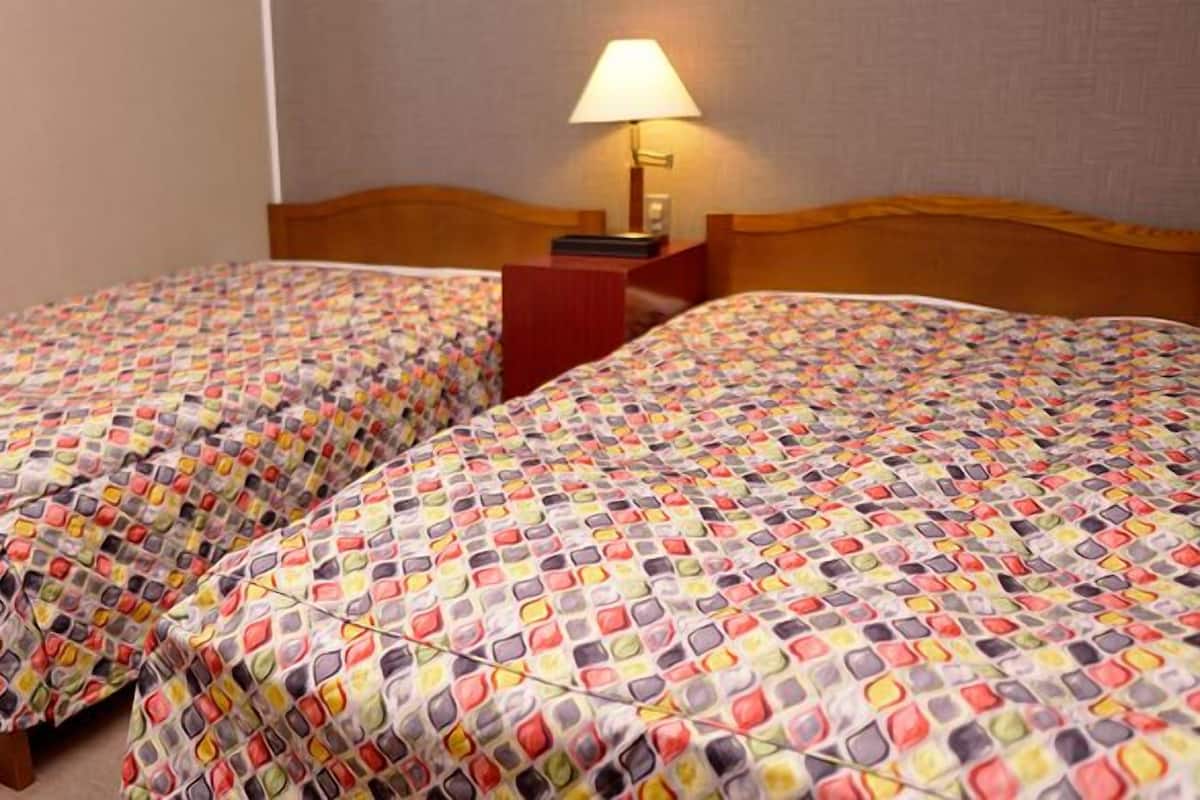 Habitación de hotel con dos camas, cada una con una colcha estampada, un cabecero de madera y una mesita de noche con lámpara.