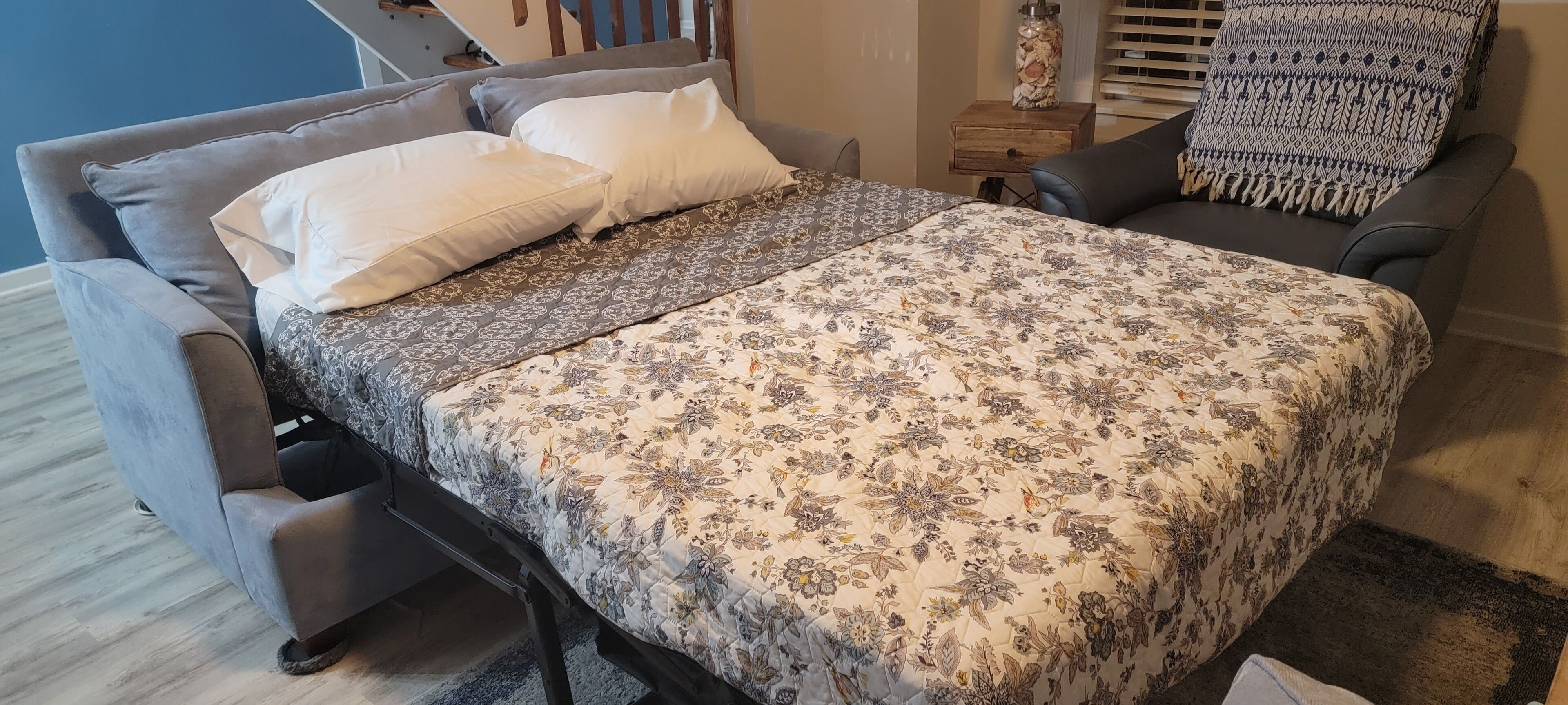 A bedroom with a bed, two armchairs, a nightstand, and a patterned bedspread.