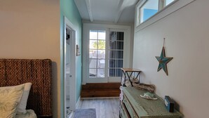 Un couloir étroit, avec un lit sur la gauche, un escalier en bois et une petite table avec des chaussures sur la droite.