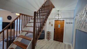 Un escalier avec des rampes en bois mène à un palier. On peut voir une horloge au mur, et il y a une porte avec une poignée décorative.