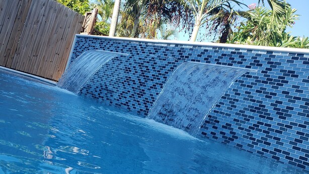 Une piscine agrémentée d’une cascade et, en arrière-plan, une clôture en bois.