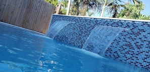 Ein Schwimmbecken mit Wasserfall und einem Holzzaun im Hintergrund.