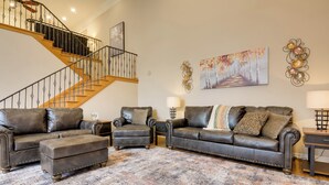 Un salon avec un escalier, des canapés en cuir, des poufs et un tapis à motifs.