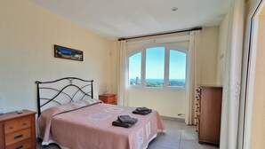 A bedroom with a bed, a nightstand, a wooden dresser, a window with a view, and a painting on the wall. - Casa Adela with private pool on walking distance to Begur. (Begur)
