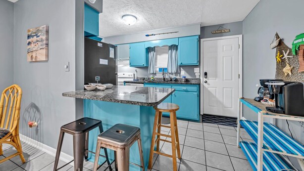 A compact kitchen with blue cabinets, a central island, and a coffee station. - Sea Turtle ~ Cozy getaway less than 1/4 of a mile from the beach! (Panama City Beach)