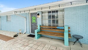 A building with a light blue brick exterior, a wooden bench, a small table, and a turtle-shaped door decoration. - Sea Turtle ~ Cozy getaway less than 1/4 of a mile from the beach! (Panama City Beach)