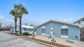 A blue building with a single arched window and a door, surrounded by a gravel driveway and a palm tree. - Sea Turtle ~ Cozy getaway less than 1/4 of a mile from the beach! (Panama City Beach)