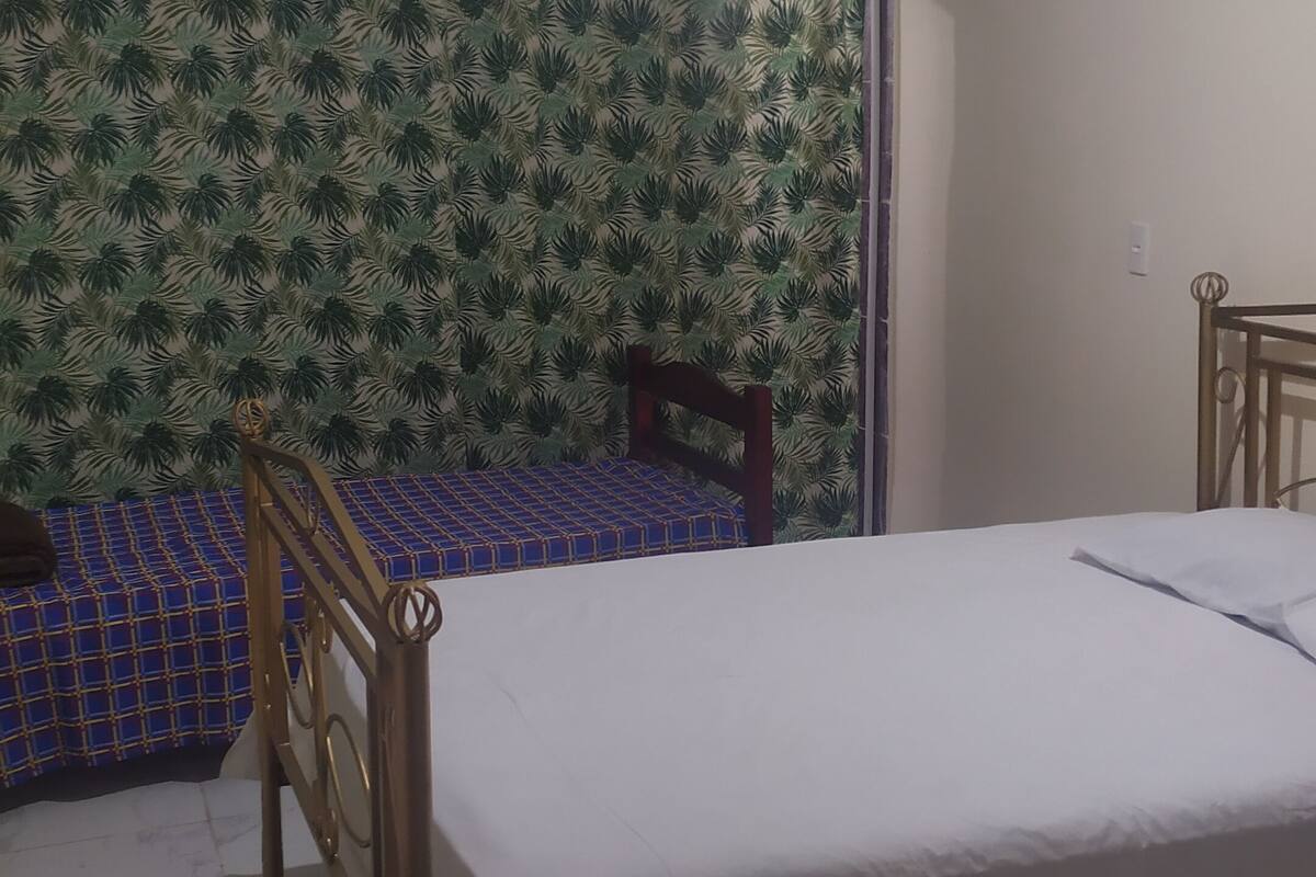 Quarto com cama, cabeceira de madeira, parede estampada e piso cerâmico.