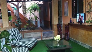 A lounge area with a wooden bench, a glass table with a vase, and a TV on a wall. - Hostel Vila Bela (Brasília)