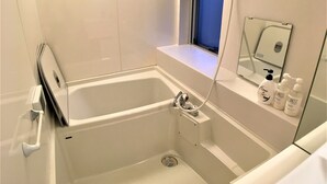 A bathroom with a bathtub, a handheld showerhead, a window, and toiletries on the counter. - Higashi-Gokencho M-building 2F (Tokyo)