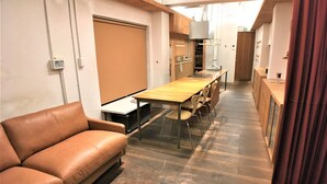A modern kitchen with a wooden table and chairs, a sofa, and a sliding door. - Higashi-Gokencho M-building 2F (Tokyo)