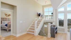 Une pièce spacieuse avec un plancher en bois, un escalier menant à un balcon et un lit agrémenté d’une literie à motifs floraux.