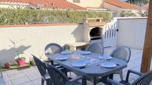 Une terrasse avec une table dressée pour quatre personnes, entourée de chaises et agrémentée de plantes en pot.