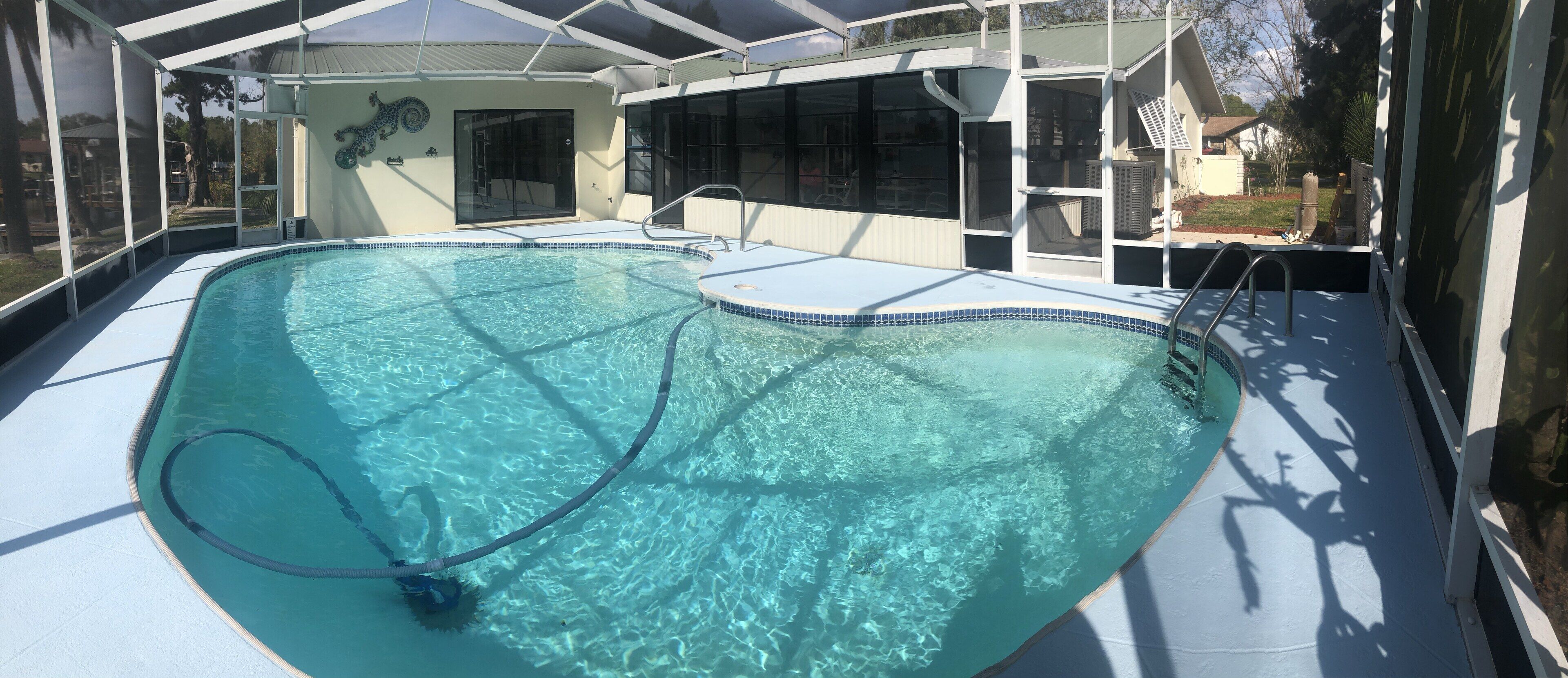 A swimming pool with clear water, surrounded by a covered area with a roof and glass walls.