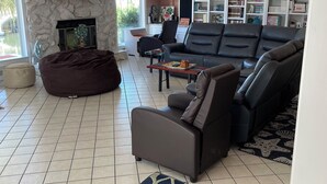 A spacious living room with a stone accent wall, a fireplace, a large bookshelf, and a modern ceiling fan. - Spacious 3 BR 2 Bath  House On Deep Canal With Screened Heated Pool  (Crystal River)