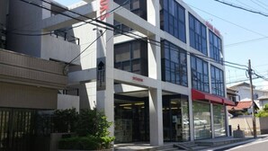 Un edificio moderno con fachada de vidrio, un toldo rojo y señalización que dice 'Yotsuyan'.